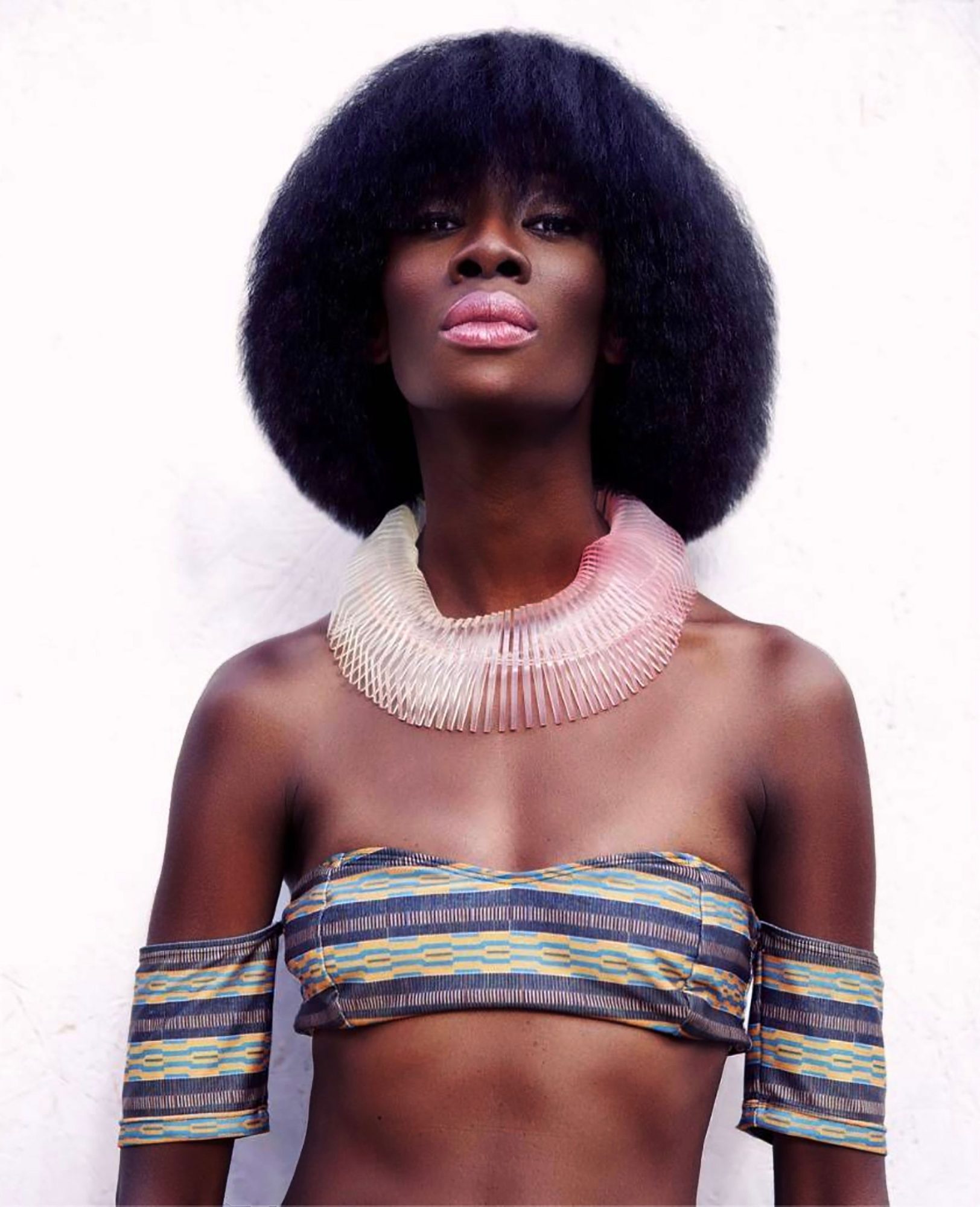 Woman with an afro wearing a woven collar on a pale ground