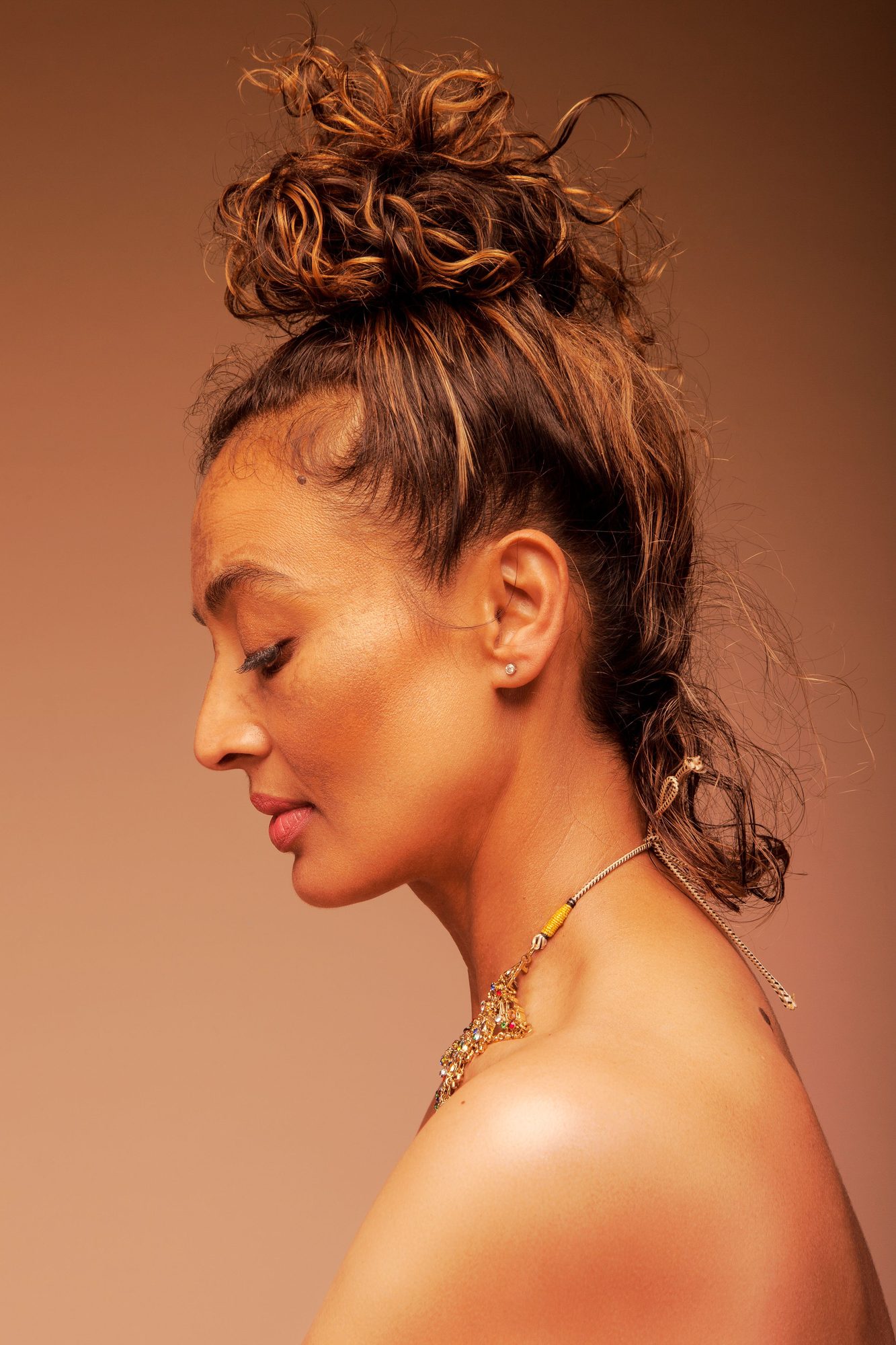 Profile of a woman with her hair up against a warm tan ground