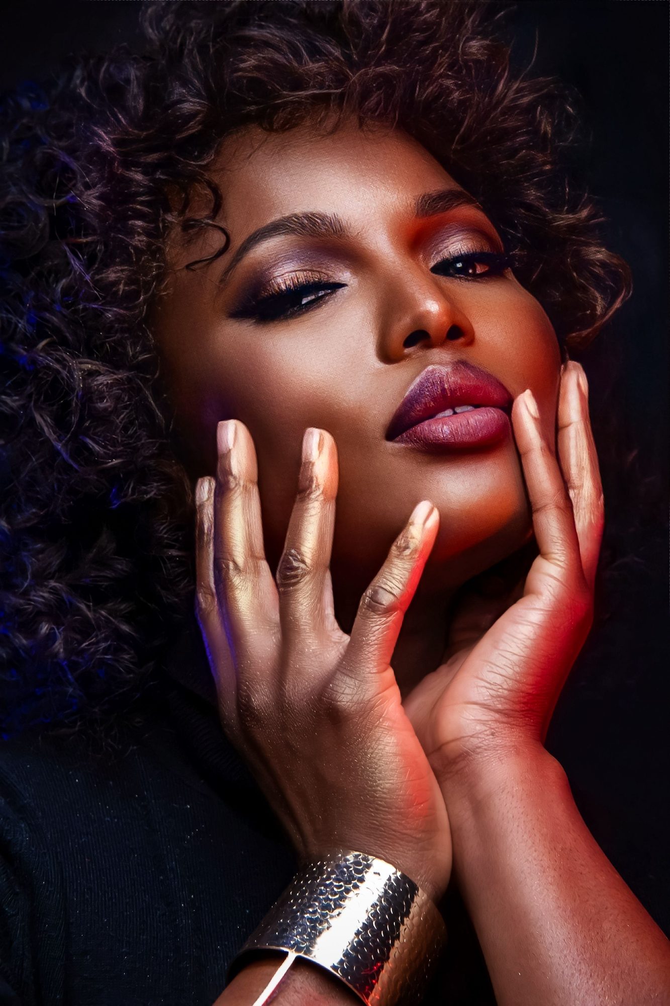 Beauty portrait of a woman with curly hair, hands at her face and a silver cuff