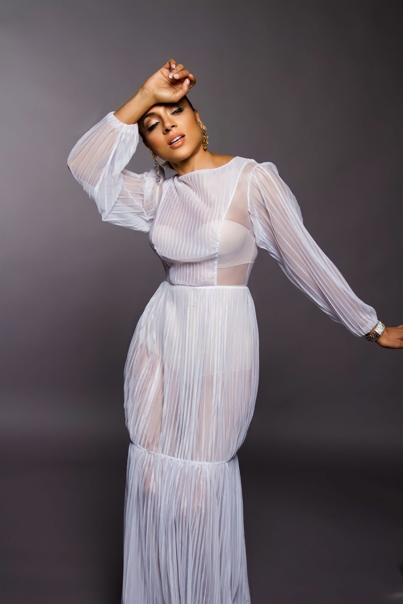 Woman in a white sheer dress posing against a grey backdrop