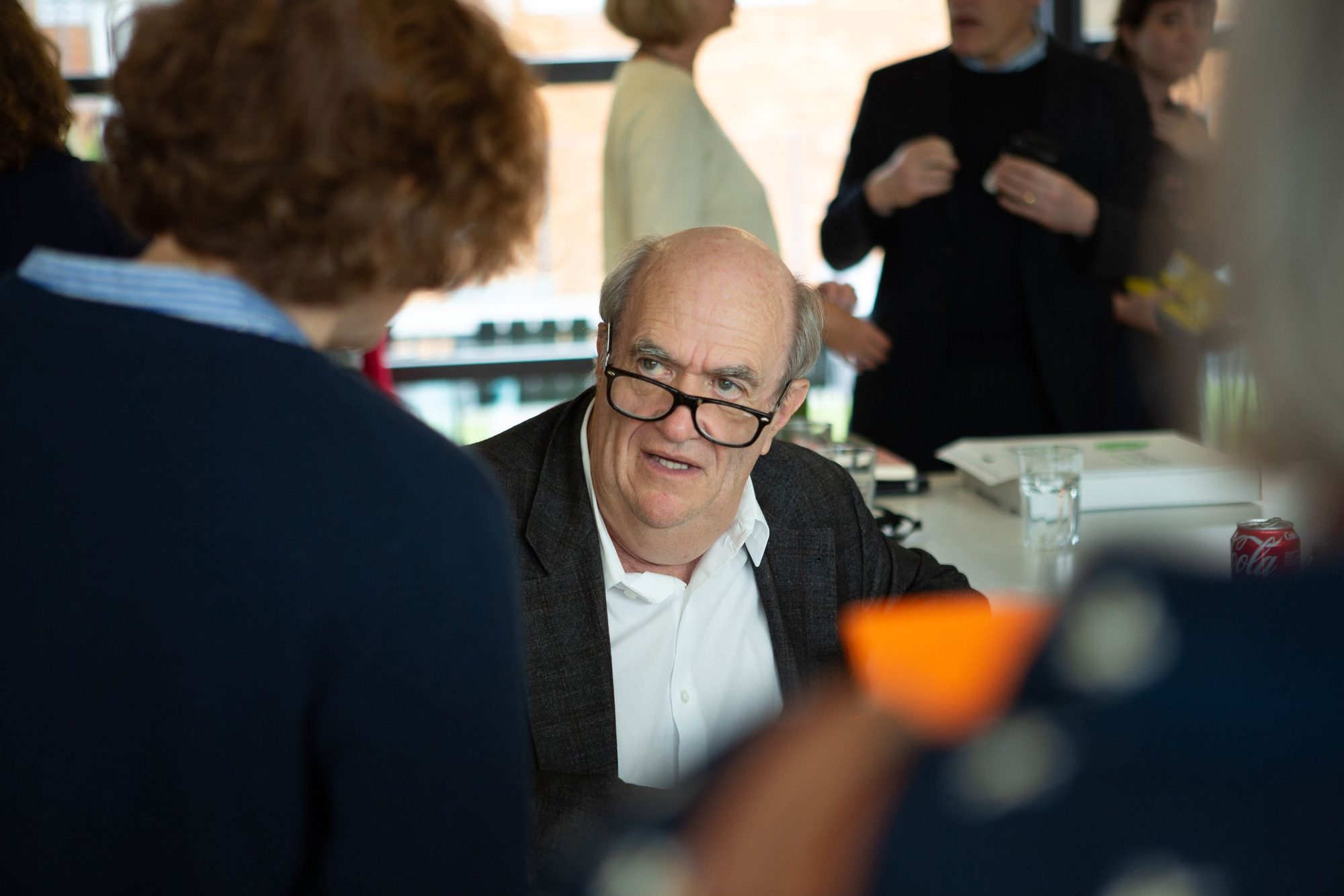 Author in glasses signing a book, guests around him