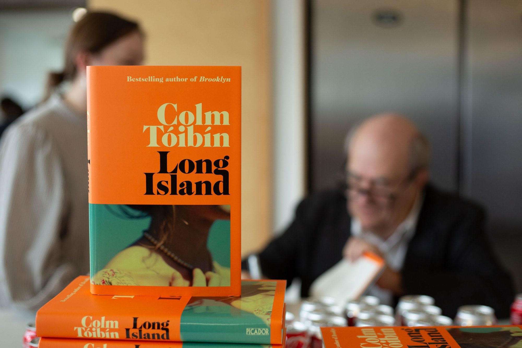 Author signing books at a table stacked with orange covers