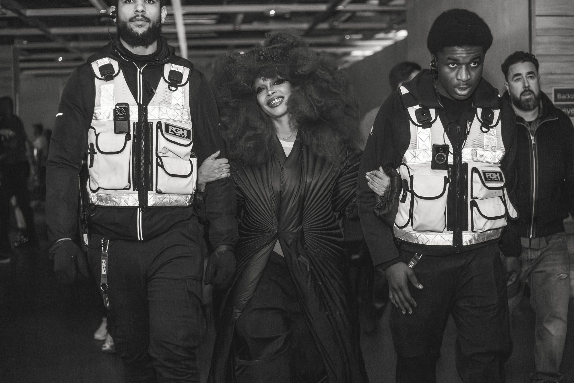 Black and white photo of a crowd moving with security staff