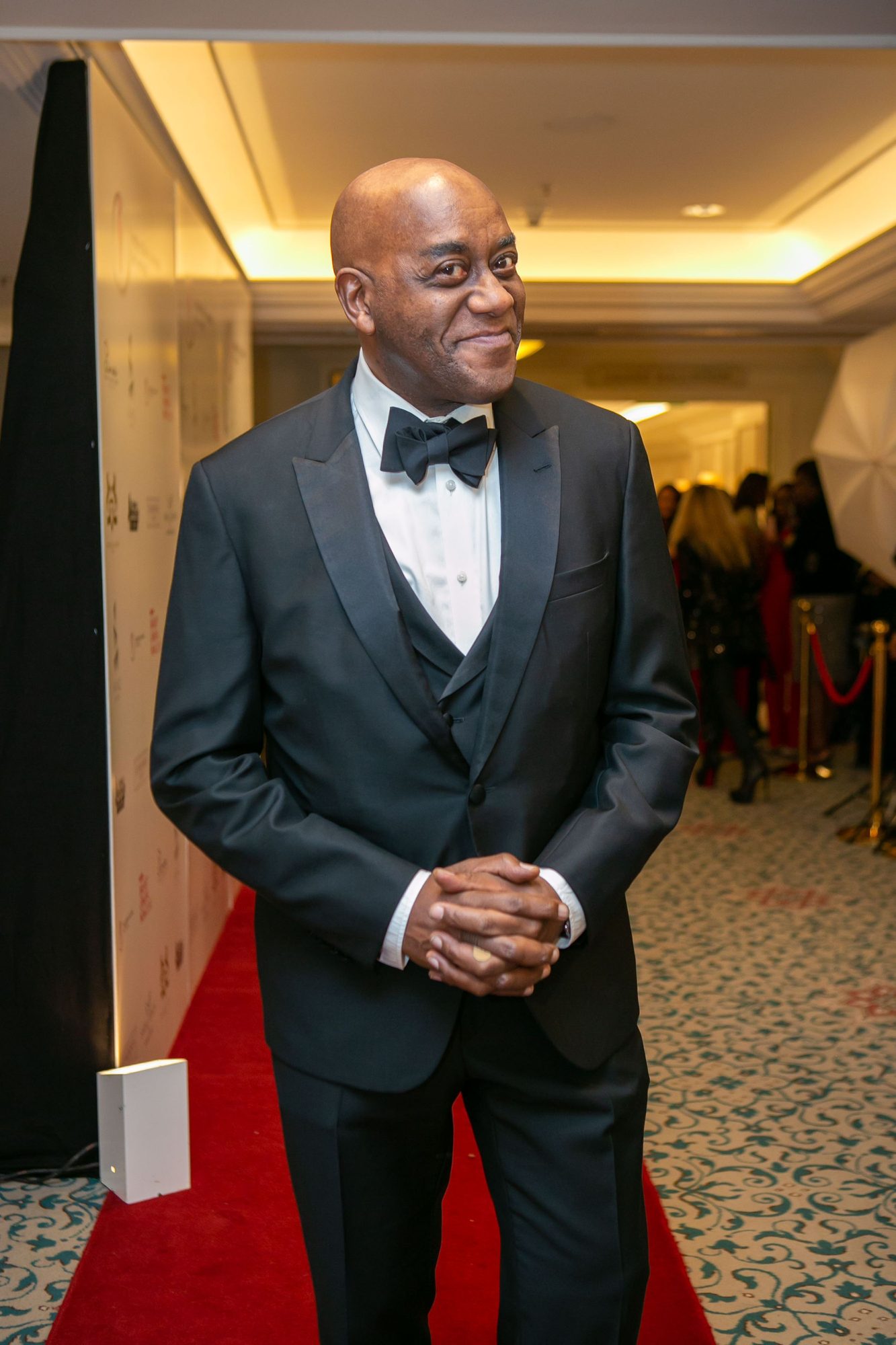 Man in a tuxedo on a red carpet in a hotel corridor