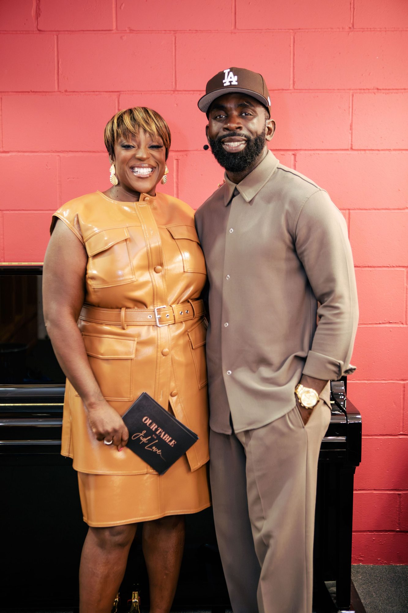 Woman in a gold leather dress and a man in beige against a red wall