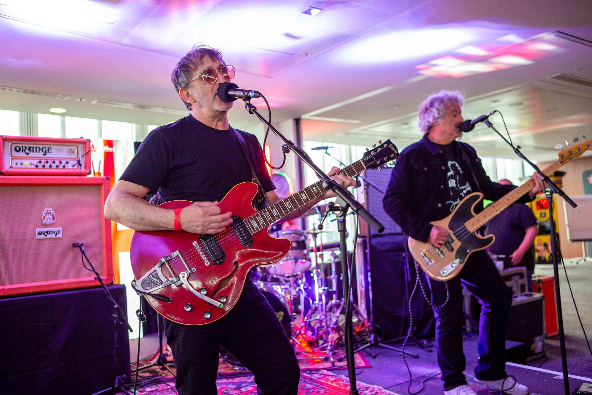 Two guitarists playing on stage under coloured lights