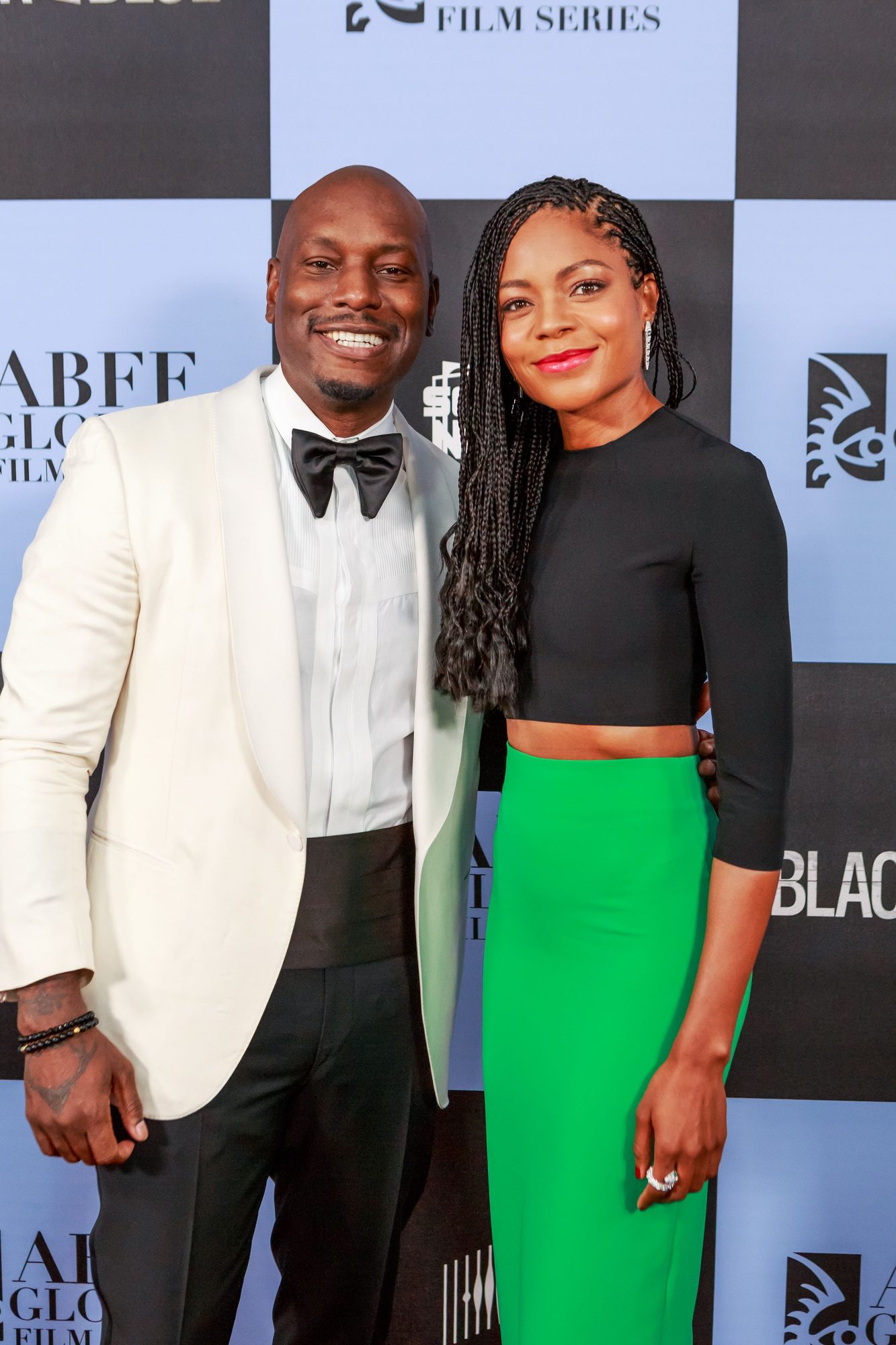 Man in a white tuxedo and woman in a green skirt at a premiere backdrop