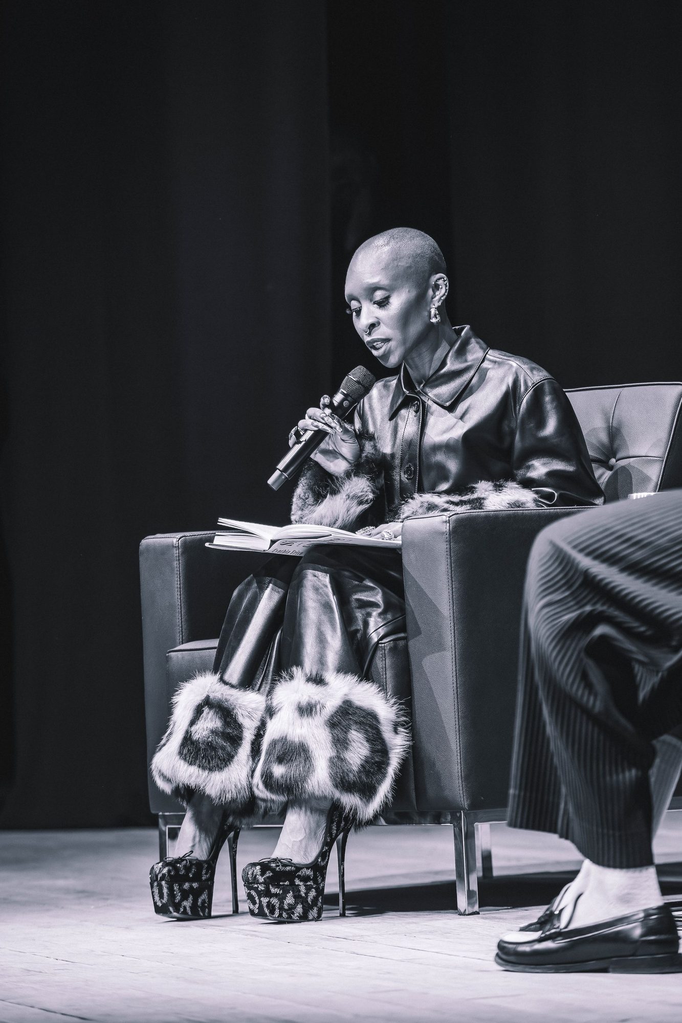 Black and white photo of a speaker seated on stage with a microphone