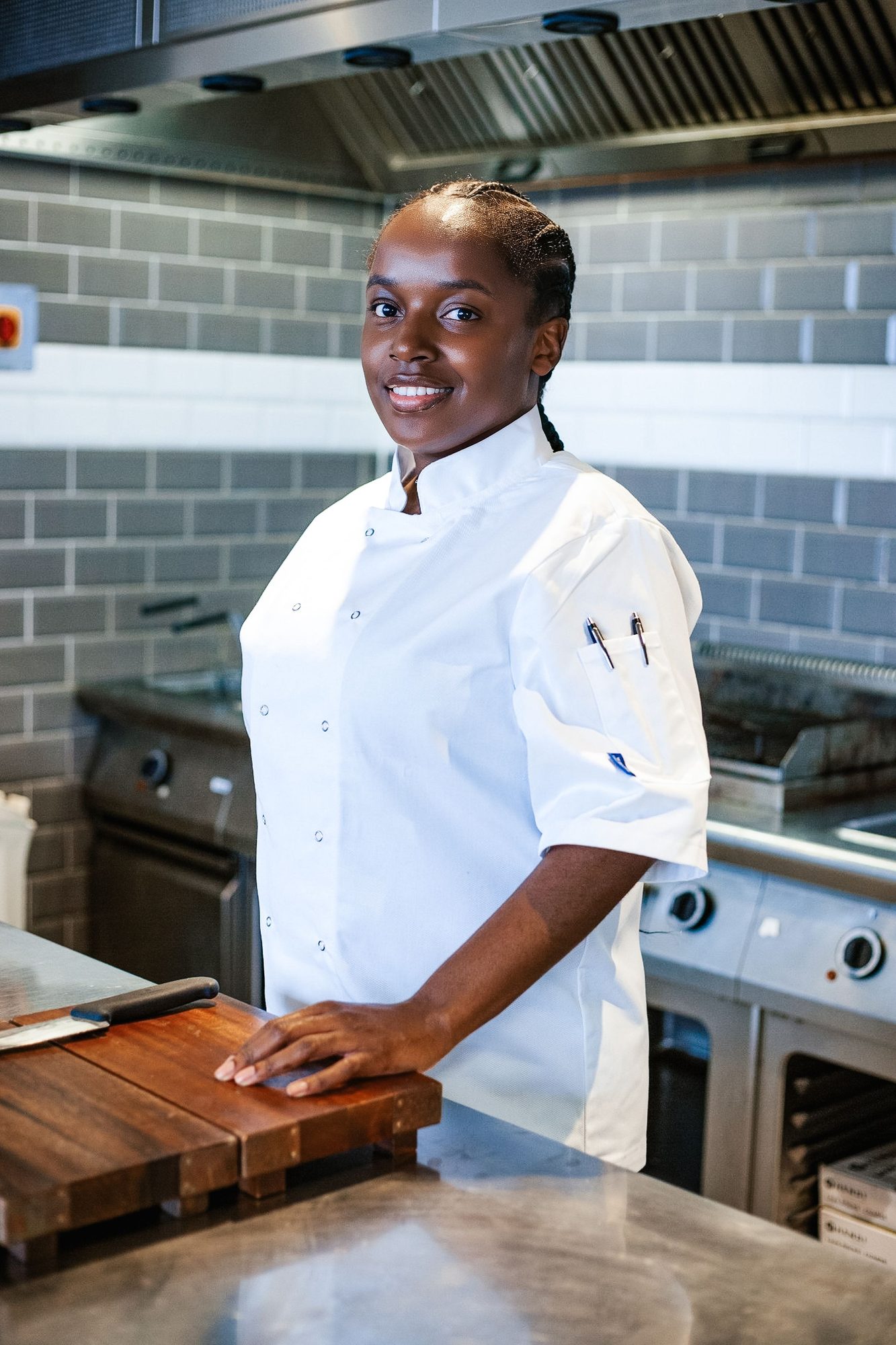 Chef in whites standing at a kitchen counter with a chopping board