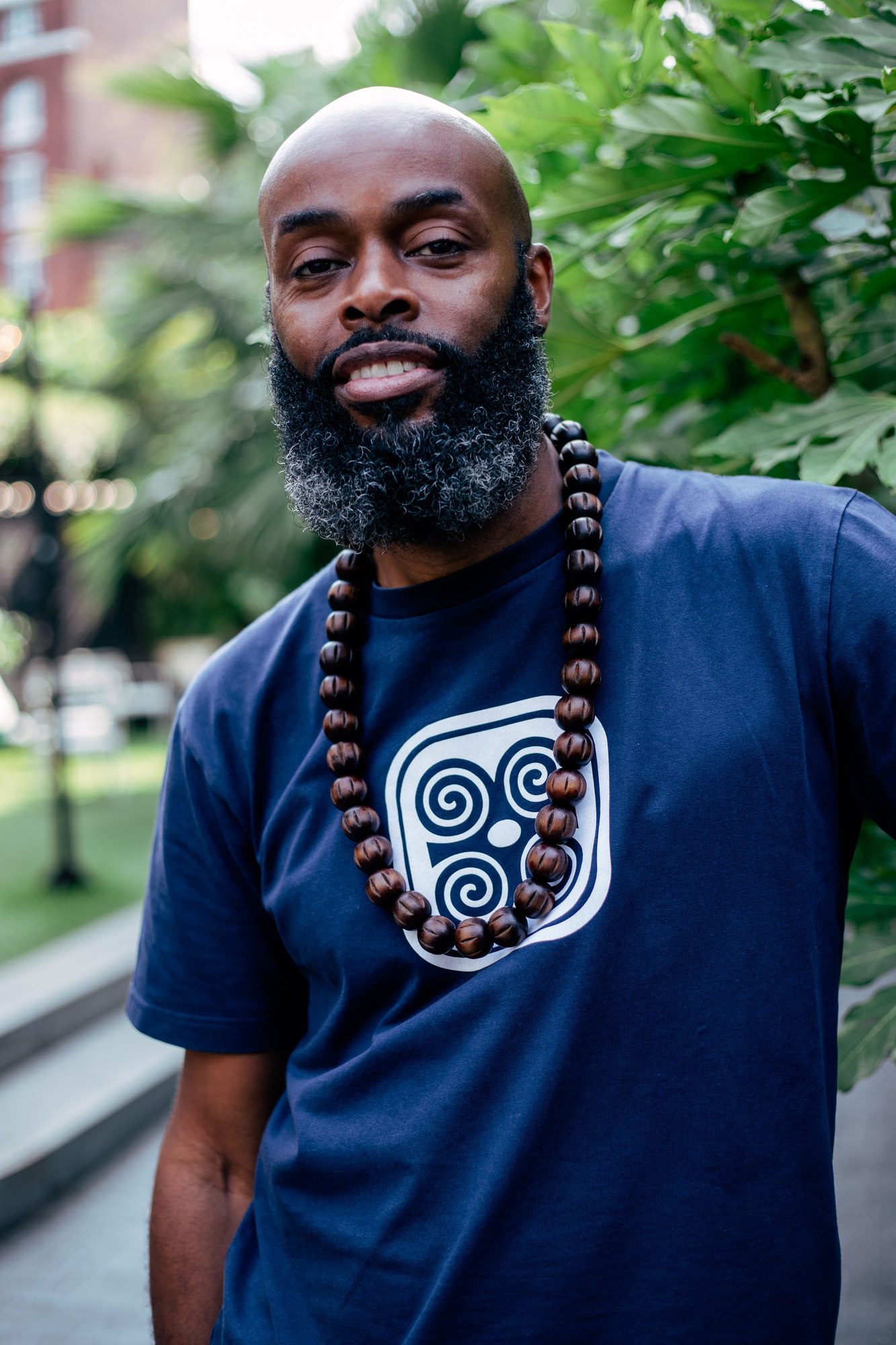 Bearded man in a blue t-shirt and beaded necklace among trees