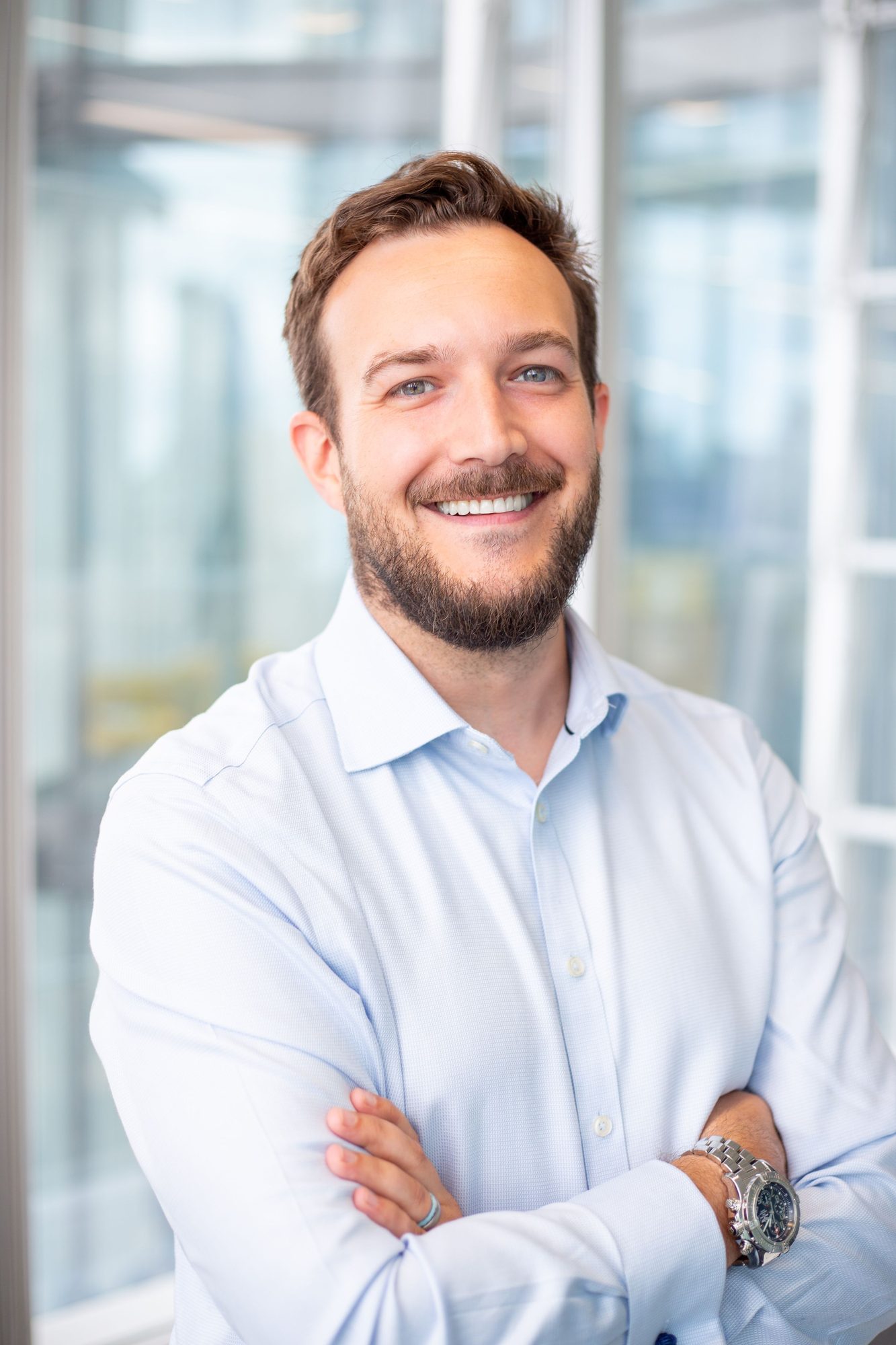 Smiling man in a light blue shirt with arms folded in an office