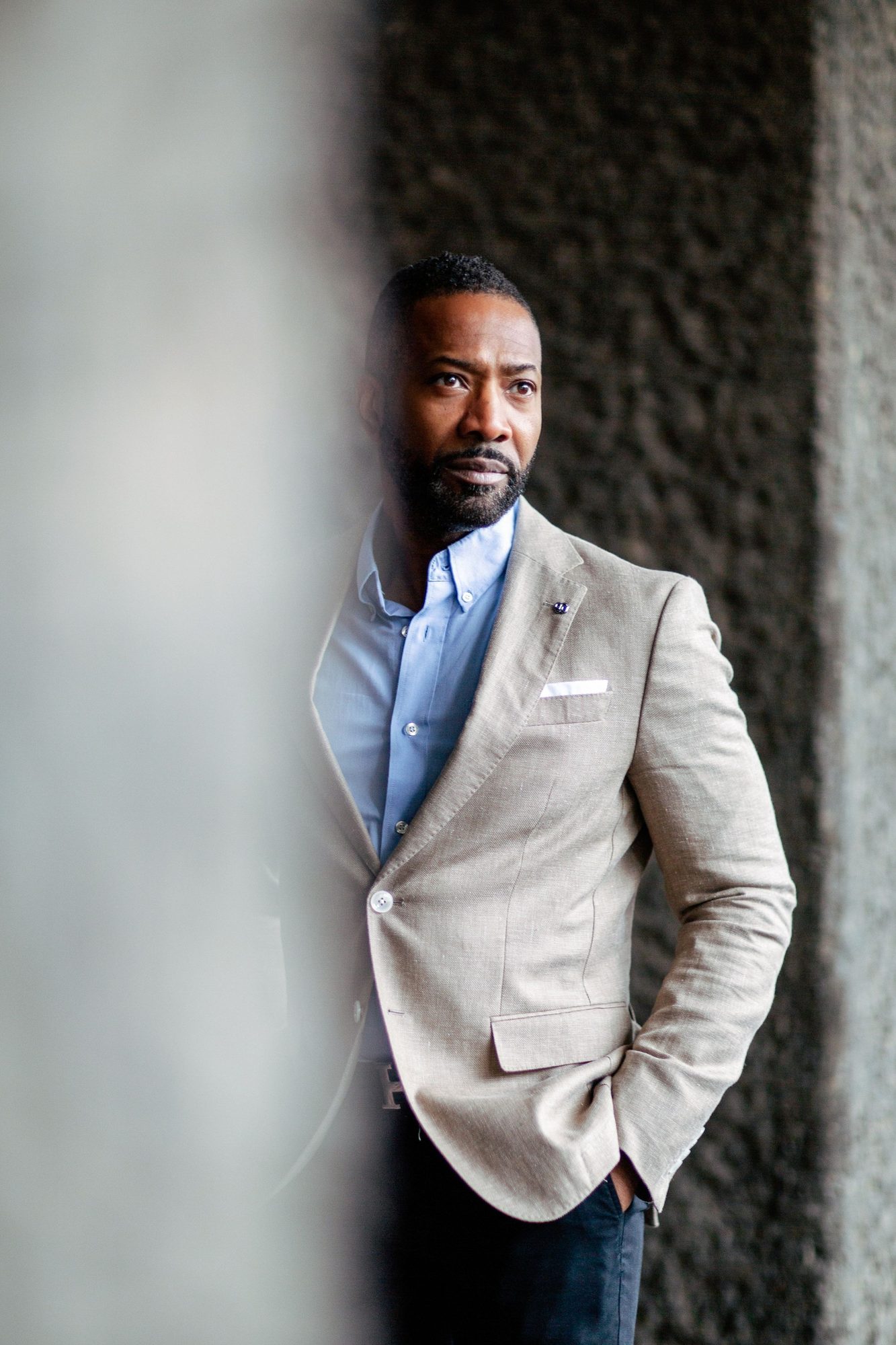 Man in a grey blazer and blue shirt leaning on a concrete wall