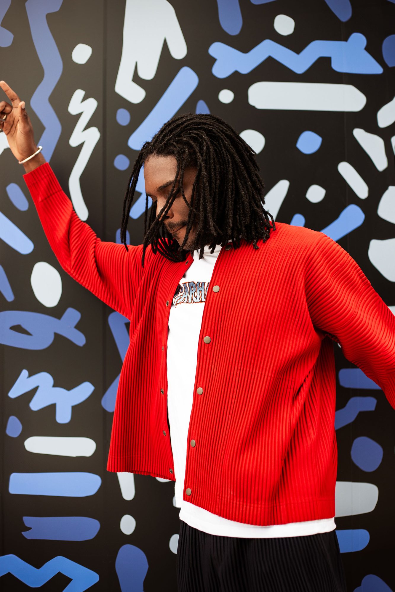 Man in a red cardigan posing against a patterned mural