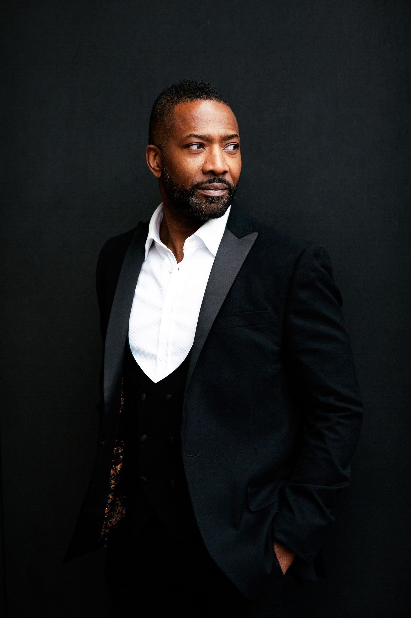 Man in a black tuxedo against a black backdrop