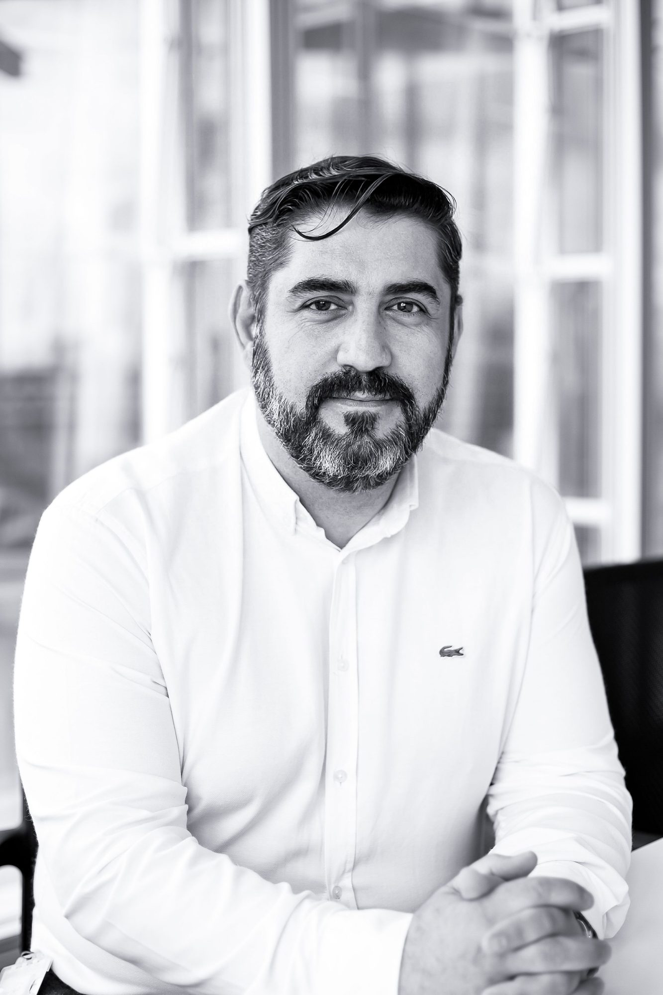 Bearded man in a white shirt sitting by a window