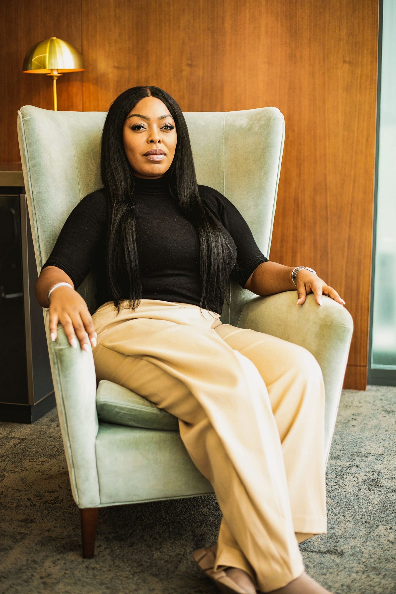 Woman in a black top and cream trousers sitting in an armchair