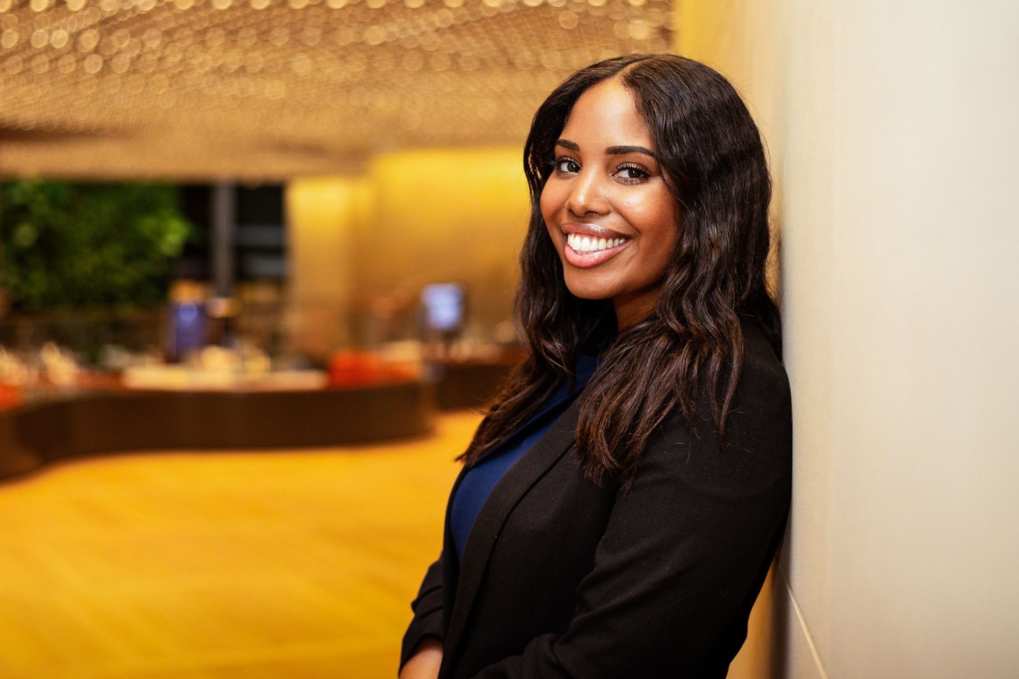 Woman in a black blazer leaning on a pillar in a warm hotel lobby