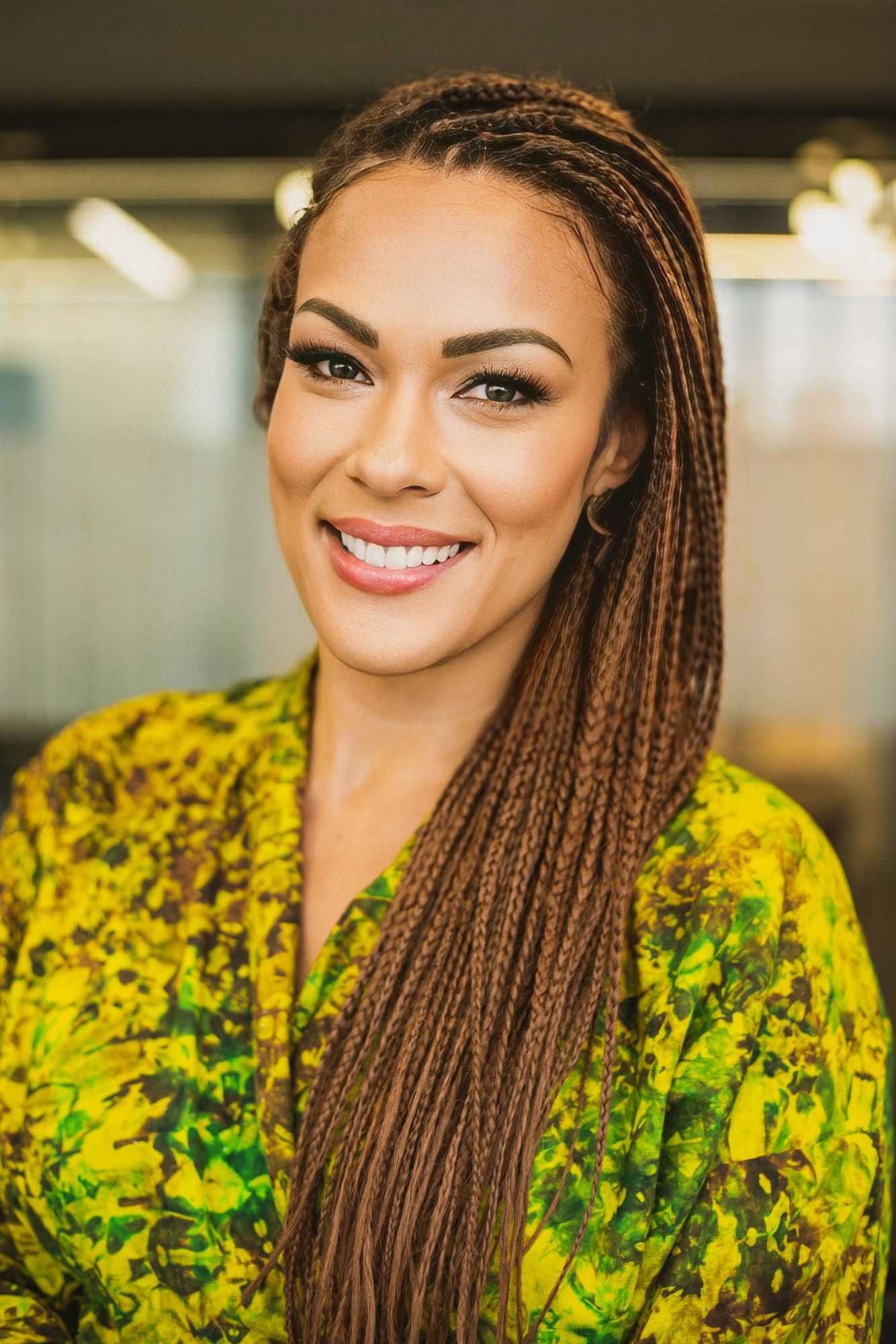 Smiling woman with long braids in a yellow and green print top