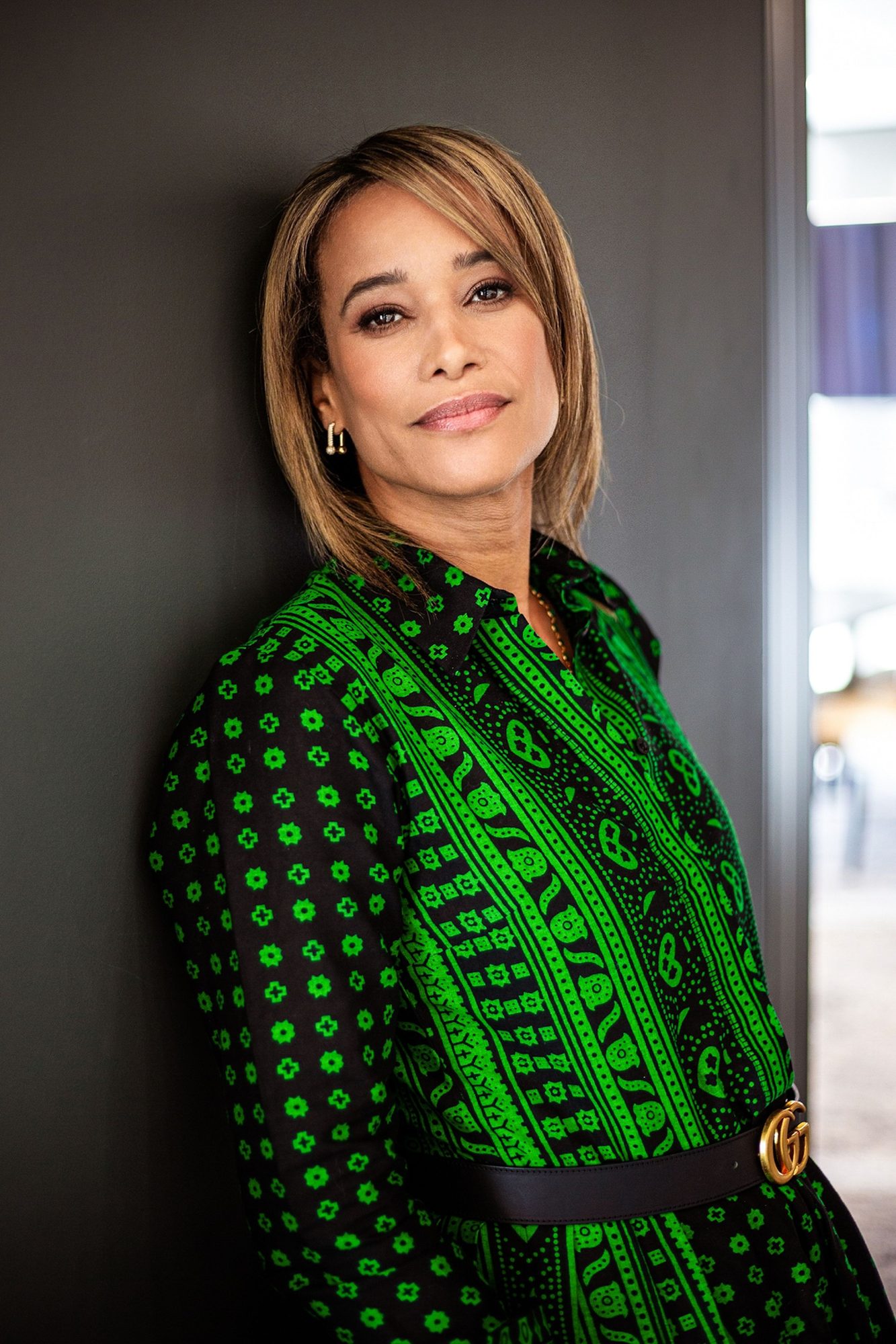 Smiling woman in a green patterned dress against a grey wall