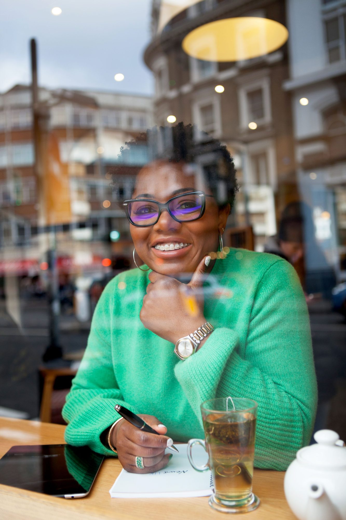 Woman in a green jacket writing at a cafe table by the window