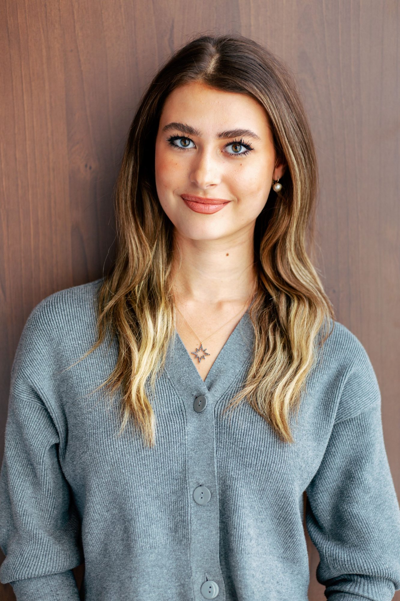 Woman in a grey cardigan against a wooden wall