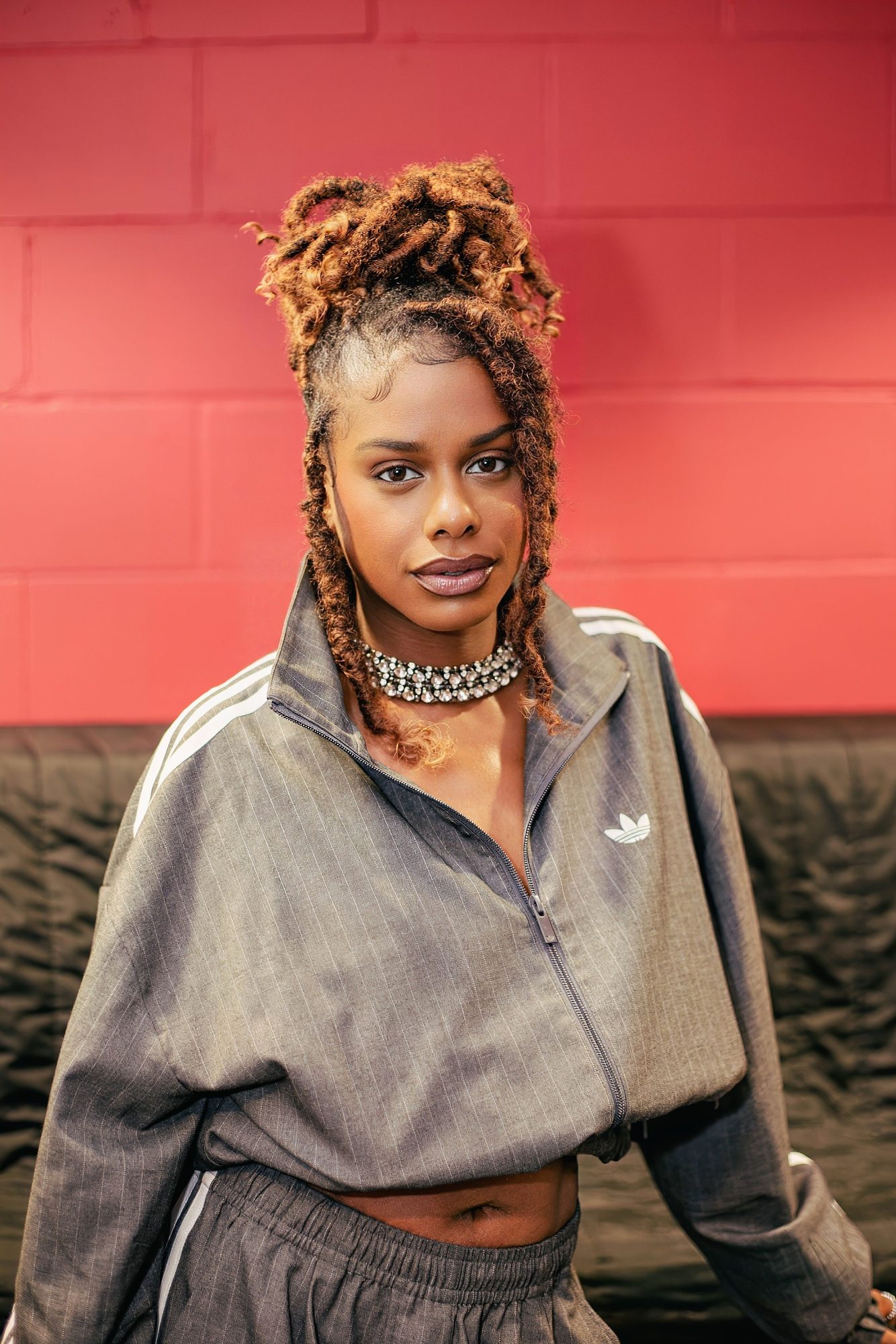 Woman with locs in a grey track top against a red wall