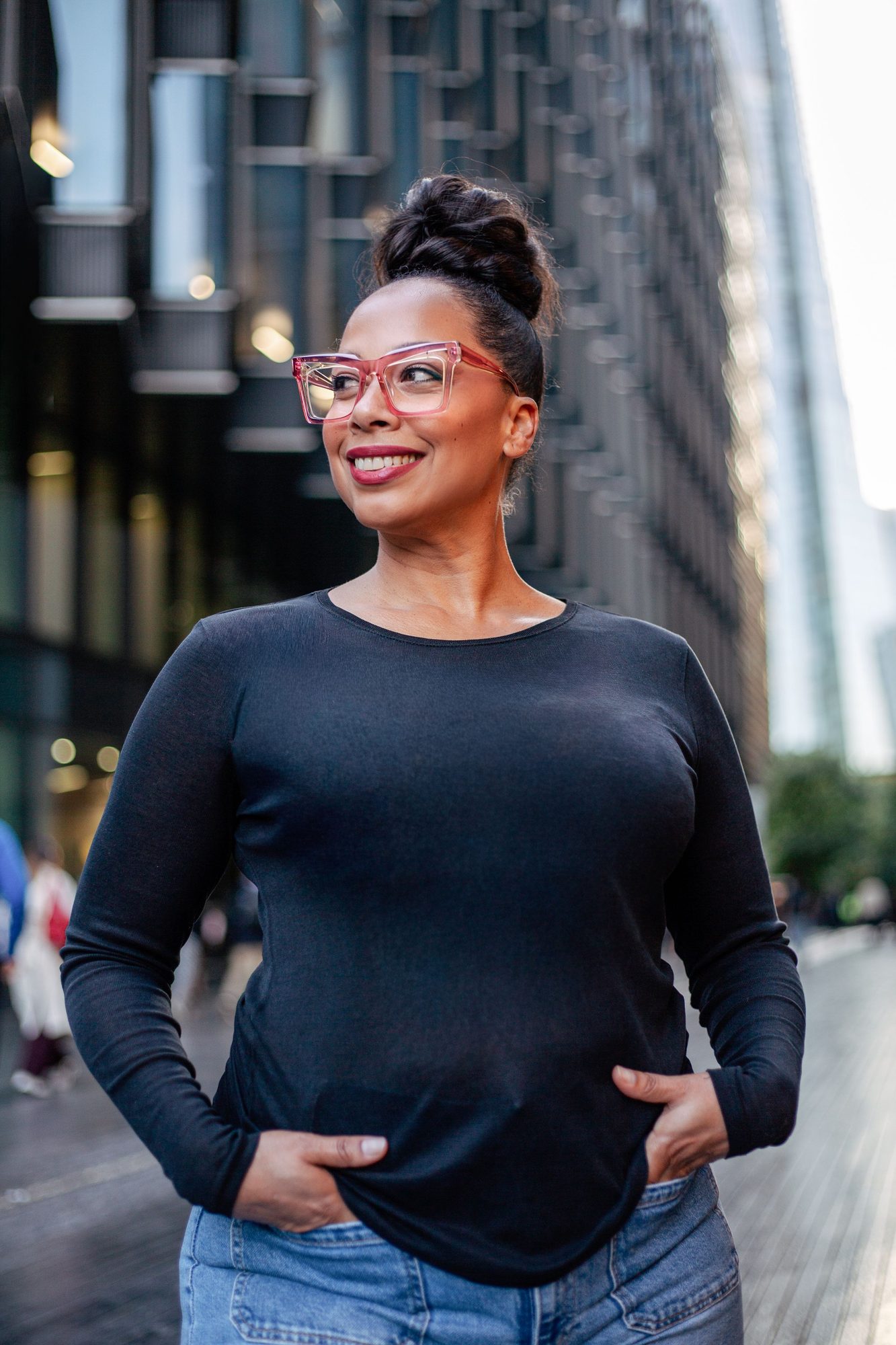 Woman in a navy jumper with her hands in her pockets on a city street