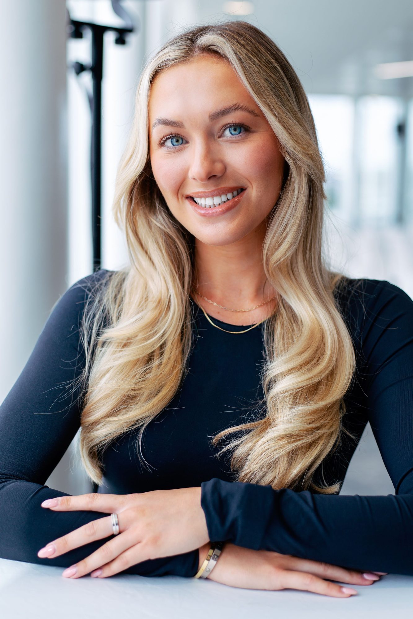 Blonde woman in a navy top leaning on a table in a bright room
