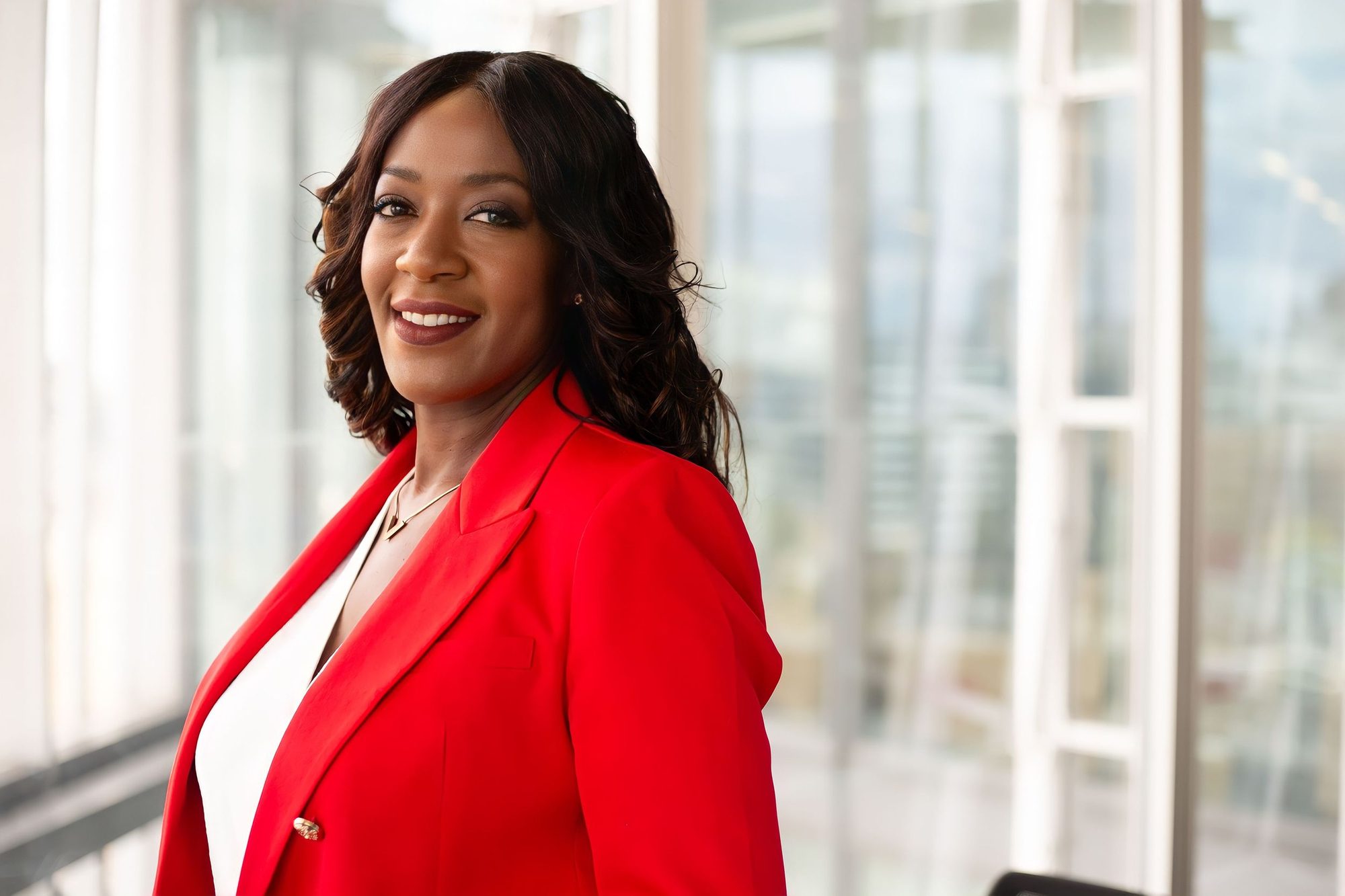 Smiling woman in a red blazer beside tall windows