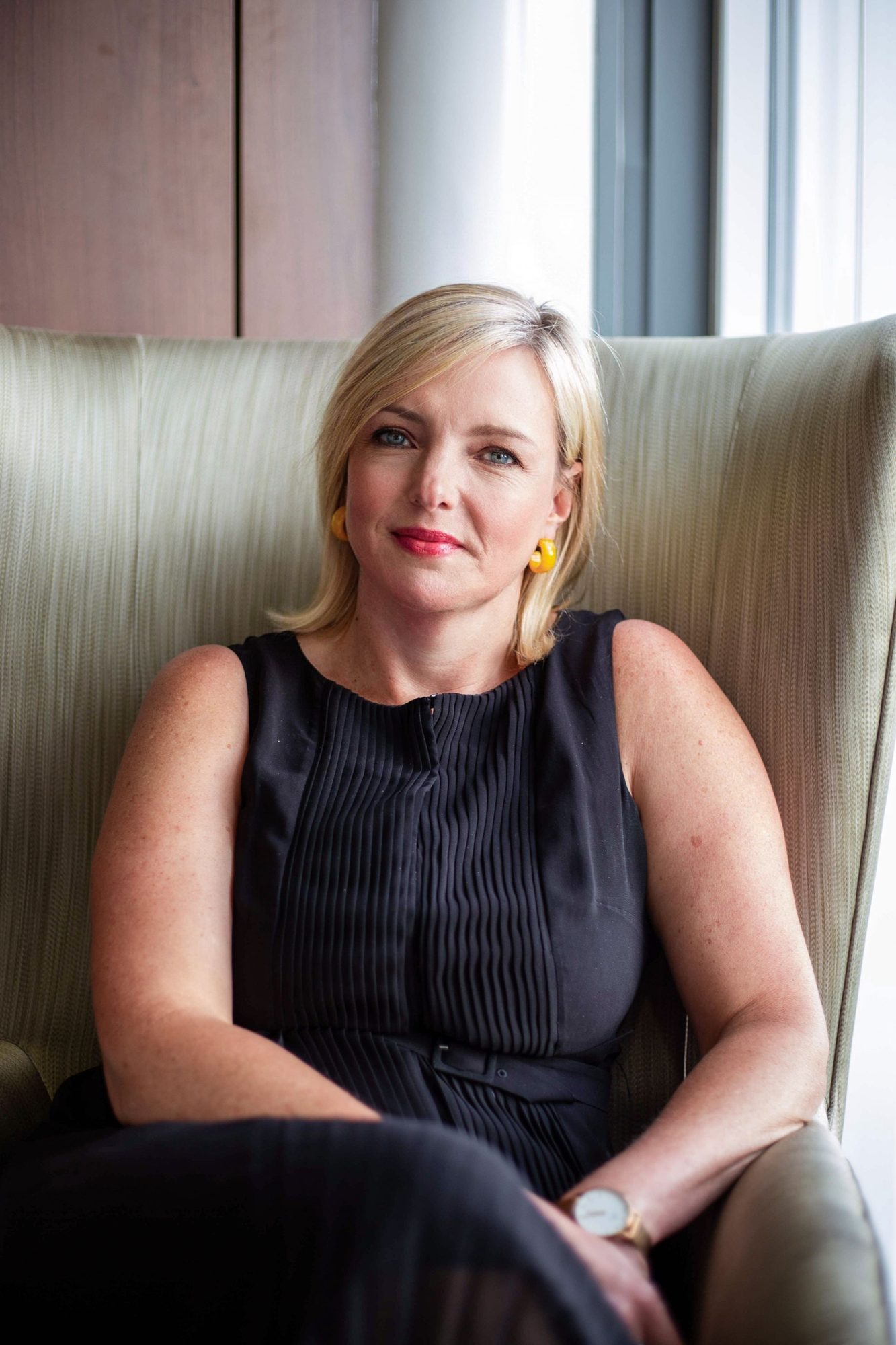 Blonde woman in a black dress seated in a cream armchair
