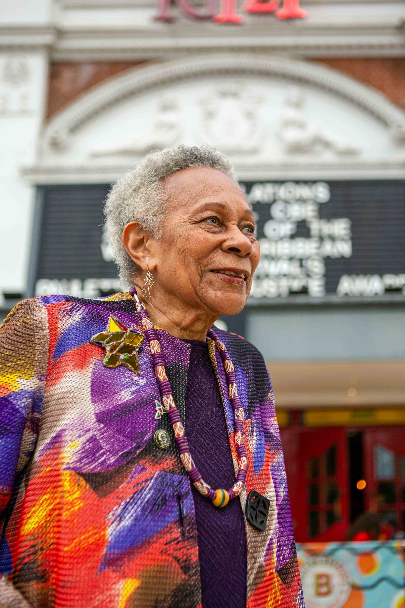 Older woman in a colourful print jacket outside a theatre