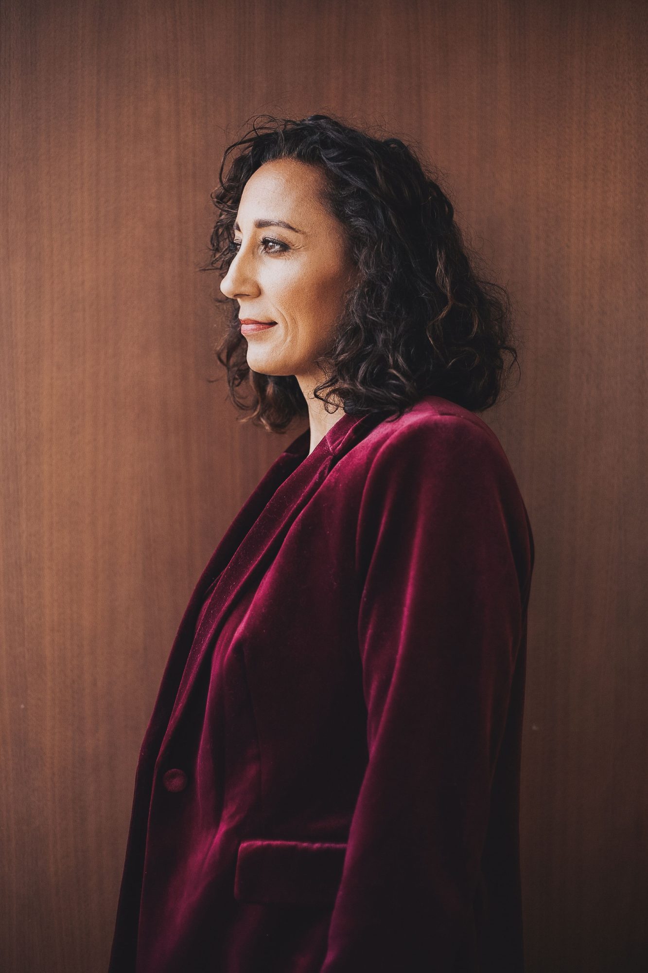 Woman in a burgundy velvet blazer in profile against warm wood
