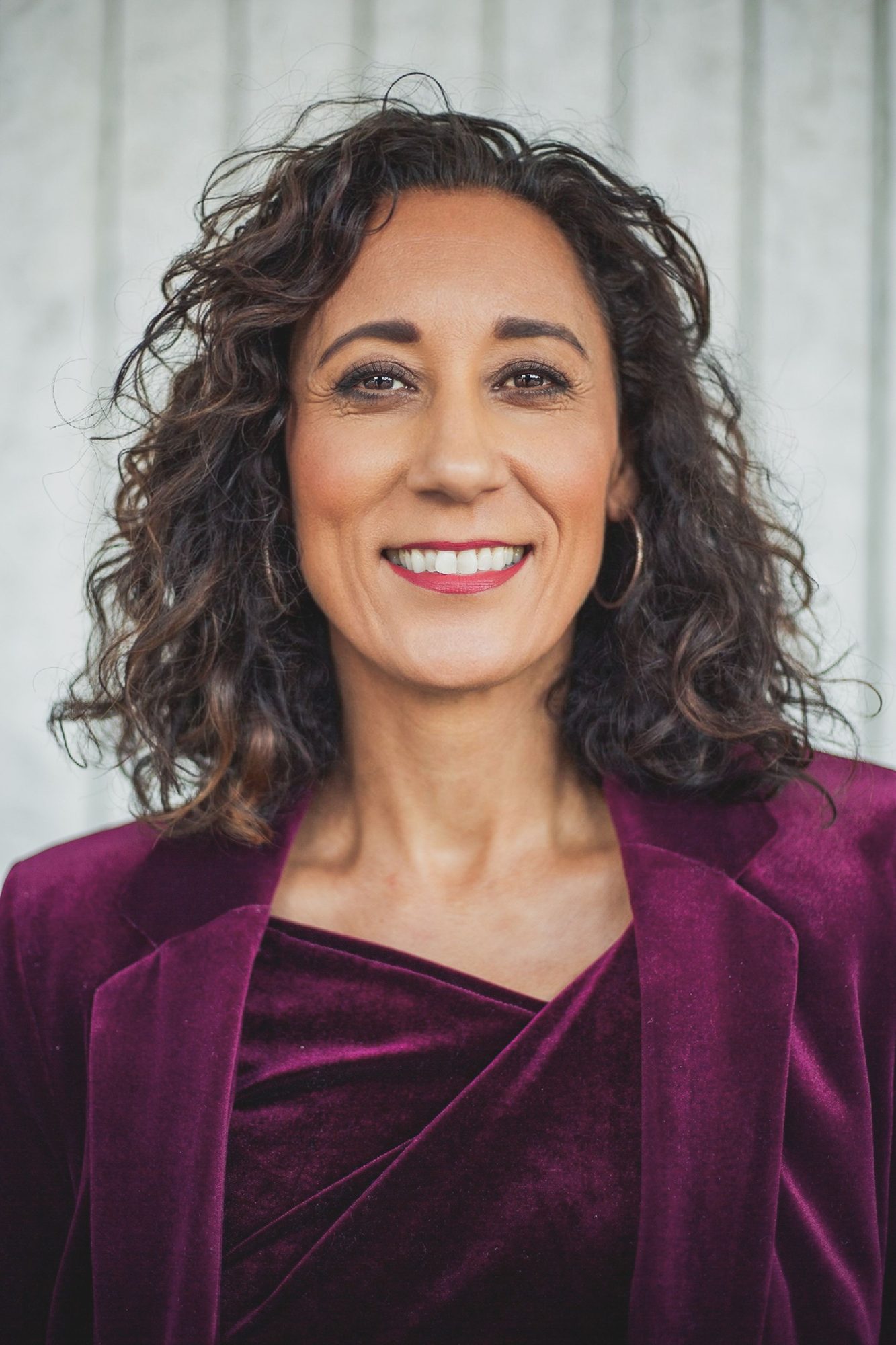 Smiling woman with curly hair in a burgundy velvet blazer